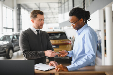 Dealer with male customer signing documents at auto salon. Bearded man in buying new vehicle at car center