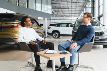 Fototapeta premium manager car salesman in car dealership signing contract at table with male buyer