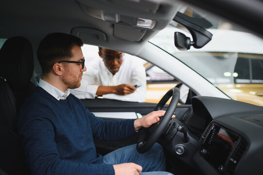Male car dealer helps customer choose car in car dealership. Man buys new car