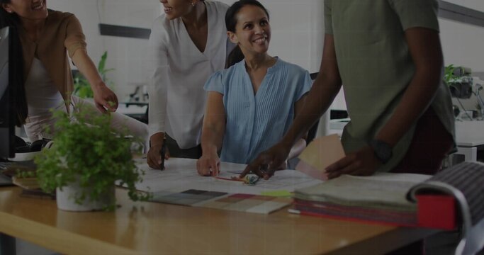 Reviewing women designers examining blueprints at table in workspace, with swatches and plant