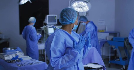 Adjusting gloves surgical nurse in blue scrubs in operating room, with monitor and surgical lights