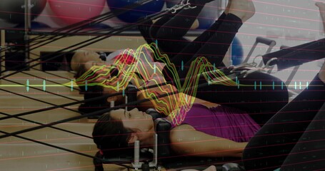 Two athletic women on reformers in Pilates studio, pushing legs pulling straps with exercise balls