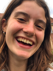 Young woman smiles brightly outdoors, showcasing joy and happiness amidst a natural setting