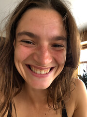 Smiling young woman with long hair enjoying a moment of joy indoors during daytime with natural light illuminating her face