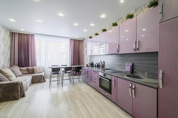 modern kitchen with lilac cabinets, gray countertops, and a dining area near a window. A cozy sofa adds a living space
