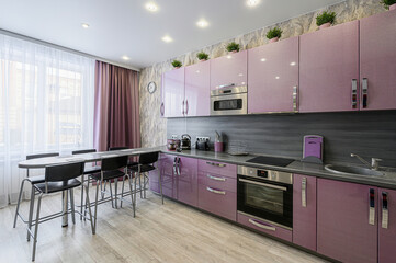 Modern kitchen features lilac cabinets, a sleek grey countertop, and bar-style seating by a bright window
