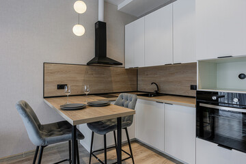 modern kitchen featuring white cabinets, wood accents, black fixtures, and gray chairs at a small dining table. Globe pendants add a stylish touch