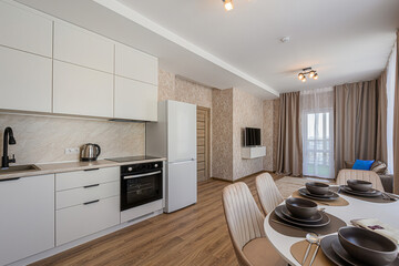 Modern kitchen and dining area with white cabinets, a round table set for dinner, and warm, neutral tones throughout the space