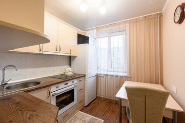 cozy kitchen with beige cabinets, dark countertops, and a dining area near a window. Appliances include a stove, oven, and refrigerator