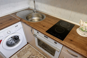 compact kitchen area with a washing machine, sink, oven, and cooktop, all neatly arranged under...