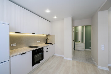 modern kitchen with white cabinets, a stone countertop, and black fixtures. An open hallway leads to a green-accented room