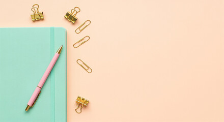 Mint green notebook with pink pen and gold paper clips on peach background