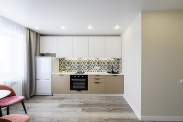 modern kitchen with white ribbed upper cabinets, beige lower cabinets, and geometric tile backsplash is shown. Pink chairs are at the edge