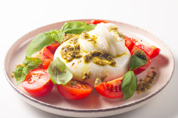 Burrata cheese caprese salad with cherry tomatoes, olive oil, pesto and seasoning. Fresh food concept. 