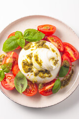 Burrata cheese caprese salad with cherry tomatoes, olive oil, pesto and seasoning. Fresh food concept. 