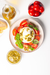 Burrata cheese caprese salad with cherry tomatoes, olive oil, pesto and seasoning. Fresh food concept. 