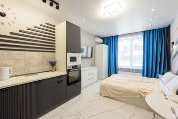 Modern studio apartment with kitchen area, bed, marble floors. Features blue curtains stylish decor
