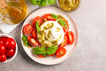 Burrata cheese caprese salad with cherry tomatoes, olive oil, pesto and seasoning. Fresh food concept. 