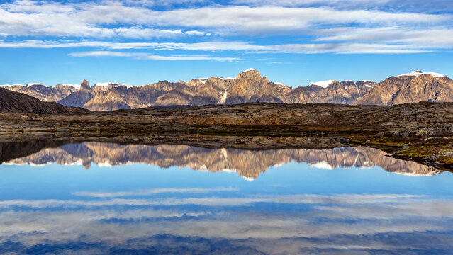 Panoramic mirror reflection of the mountain range at Bear Islands, Northeast Greenland National Park, with the Grundtvigskirken mountain peak to the left. In Ofjord, Scoresby Sund, Greenland