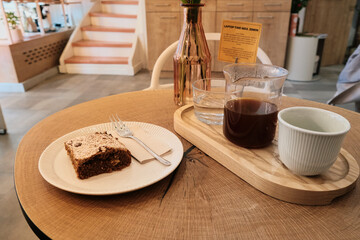 Wide shot of cozy café interior with wooden table holding coffee set and dessert, soft lighting and blurred background creating warm, inviting, and relaxed atmosphere.