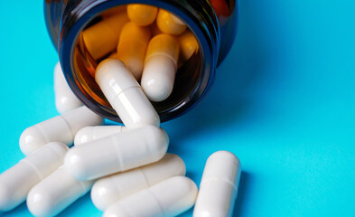 Close-up of White antibiotic capsule pills spread out of pill amber glass bottle on blue background