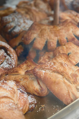 Close-up view of assorted pastries behind a bakery glass display, showcasing fresh baked goods like croissants, twists, and donuts in an inviting café atmosphere.