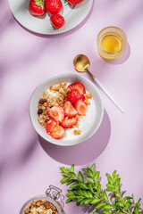 Granola or muesli with natural greek yogurt, strawberry and honey in a bowl on a bright violet background
