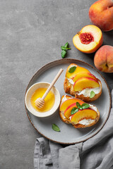 Flat lay of toast bruschetta with peach, nectarine, cream cheese or ricotta and honey on a plate on a dark background