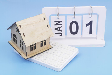 January, 1 on calendar and house model on calculator on blue background. Symbol of buy and rent...