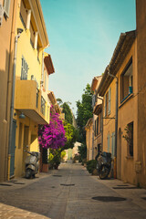 Charming sunlit street in St. Tropez with cobblestone pavement, pastel buildings, and blooming flowers