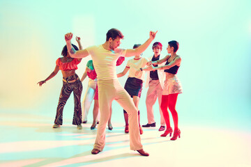 Naklejka premium Friends dancing in group celebration with retro outfits and bright lights. Concept of youth culture, parties, music events and joyful entertainment.