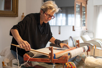 Mujer mayor parada tejiendo en telar concentrada,  medio cuerpo