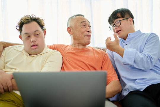 An elderly man is talking with a man with Down syndrome while holding a laptop - Powered by Adobe