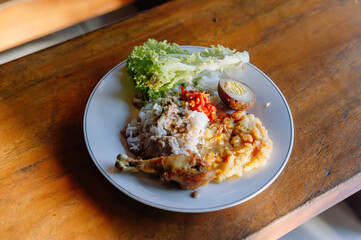 A mouth-watering plate of Nasi Campur, a traditional Indonesian mixed rice dish with chicken, egg, and vegetables on a wooden table