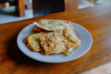 Crispy and delicious Tempe Mendoan, a traditional Indonesian fried tempeh, served on a white plate on a rustic wooden table