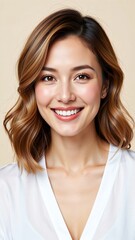 Fototapeta premium Beautiful young Asian woman with wavy brown hair and white blouse smiling warmly isolated on beige background for marketing campaign, advertising, or website hero image with copy space