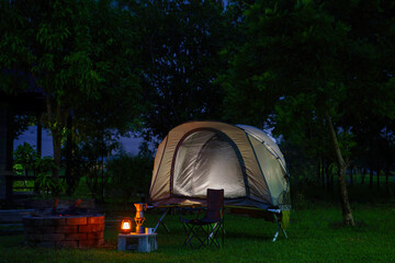 Camping tent and gas lantern on the grass next to a wood stove in the forest, with outdoor coffee-making facilities in a forest camping area