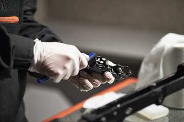 Caucasian middle aged man wearing gloves using tool to adjust mechanical component on workbench, focusing on precision maintenance task with hands clearly visible