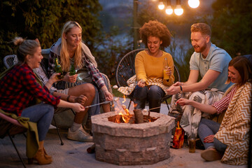 Friends sitting by the fire roasting marshmallows at night and having fun together.