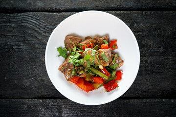 meat with paprika and asparagus in a white plate on a dark wooden background