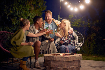 Group of friends on a chilly night, enjoying time together, drinking beer and roasting mashmallows by the fireplace.