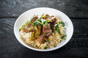 meat with rice and herbs with green chili pepper in a white plate on a dark background