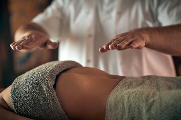 Male therapist doing reiki massage on young woman in the massage studio.