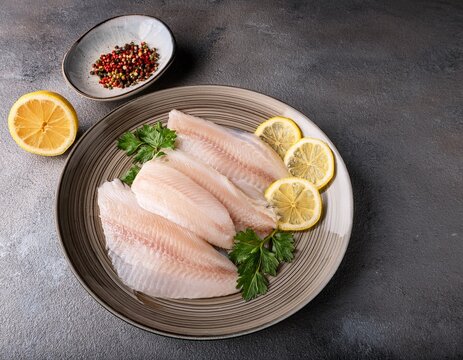 fresh pangasius fish fillet garnished with lemon and spices displayed on a plate against a textured concrete backdrop