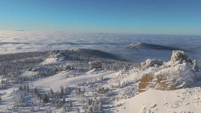 Aerial view drifts over the Sheregesh ridge as a vast cloud inversion fills the valley. Crisp winter light reveals orange cliff and glittering snow, inviting travel and ski adventure