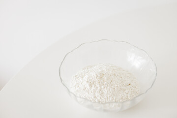 Glass bowl overflowing with white flour on a white table for cookbook