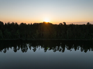 Naklejka premium Stunning aerial drone view of a serene sunrise over a forest with a perfect mirror reflection in a calm Estonian lake.