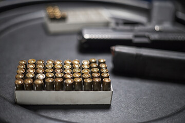 Box of handgun ammunition arranged on dark surface with blurred semi automatic pistol and magazine...