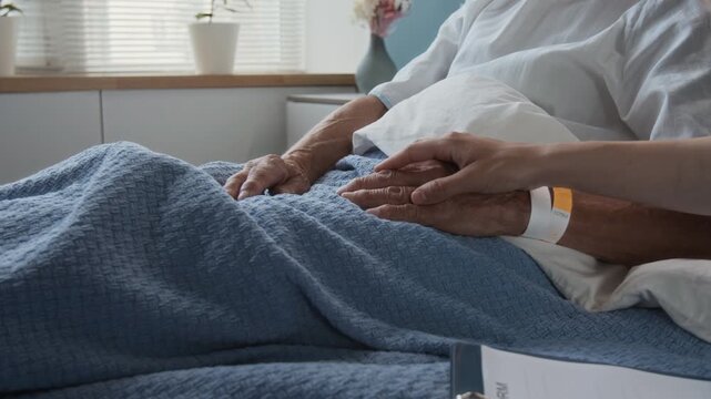 Close-up zoom in shot of unknown female doctor with medical document on clipboard comforting anonymous senior patient receiving treatment in hospital room