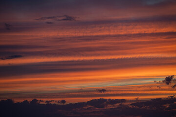 Colors blend beautifully in the sky as the sun rises, casting warm tones of orange and yellow through fluffy clouds.